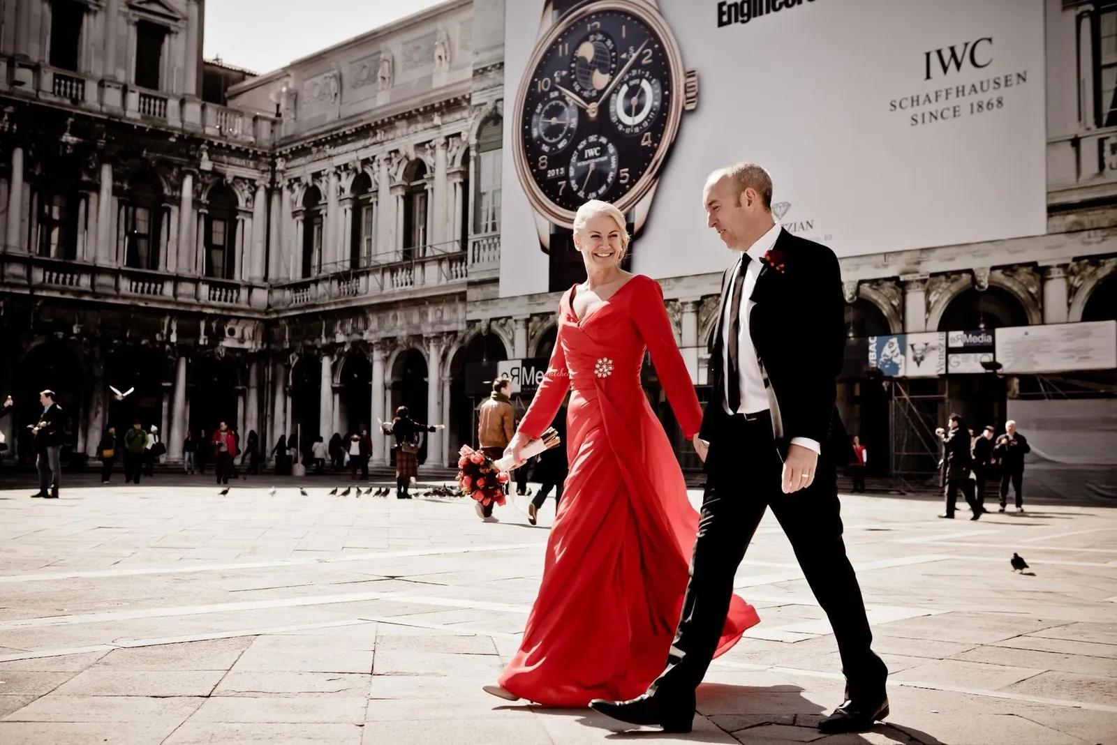 Bride in a red dress and groom walking through a city square